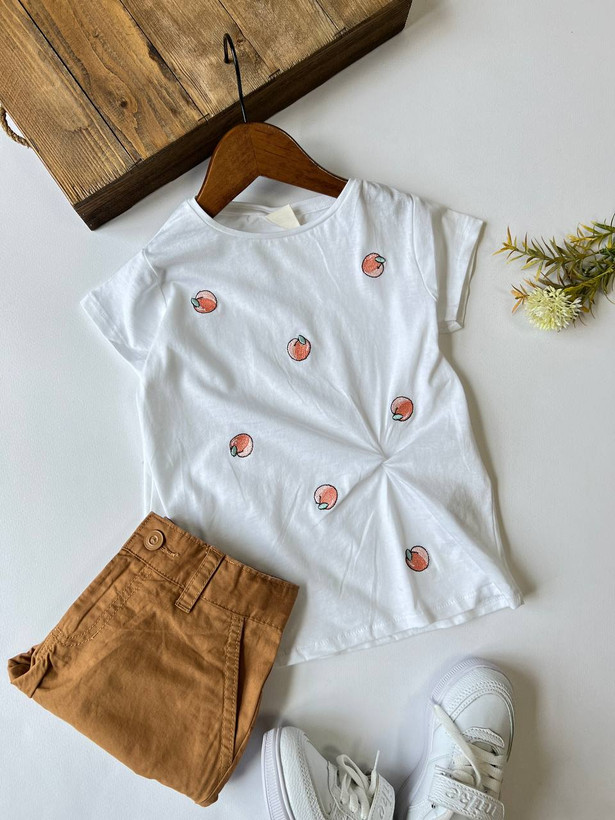 تیشرت دخترانه زارا سفید آستین کوتاه با گلدوزی برجسته طرح هلو و مدل گرهای پایین لباس